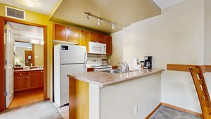 Cocina compacta con gabinetes de madera, un refrigerador blanco, un microondas, estufa y cafetera.
