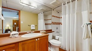 Un baño con tocador de madera, lavamanos, inodoro y zona de ducha.