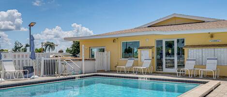 A swimming pool with lounge chairs and a building with a yellow facade.