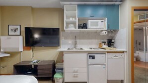 Une petite cuisine équipée d’un four à micro-ondes, d’un grille-pain et d’un évier. On y trouve également un petit réfrigérateur, un téléviseur fixé au mur et une poubelle.