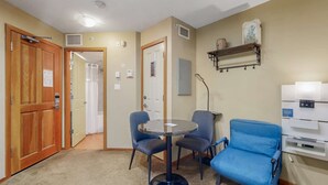 Une pièce avec une table ronde, deux chaises, un canapé bleu, des portes en bois et un mur blanc avec une étagère.