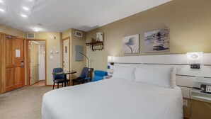 Une chambre d’hôtel avec un grand lit, deux fauteuils, un bureau avec un téléphone et des œuvres d’art accrochées au mur.