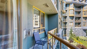 Un balcon avec une chaise, une fenêtre avec des stores et une vue sur un immeuble doté de nombreux balcons.