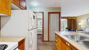 A compact kitchen with a refrigerator, stove, and sink, leading to a bedroom with a window. - Whistler - Cascade Lodge 220 (Whistler)