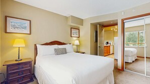 Une chambre d’hôtel avec un grand lit, deux tables de chevet avec des lampes, une commode et une vue sur la chambre voisine.