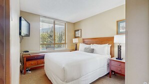 A hotel room with a large bed, bedside lamps, a desk with a computer, and a TV mounted on the wall. - Whistler - Cascade Lodge 212 (Whistler)