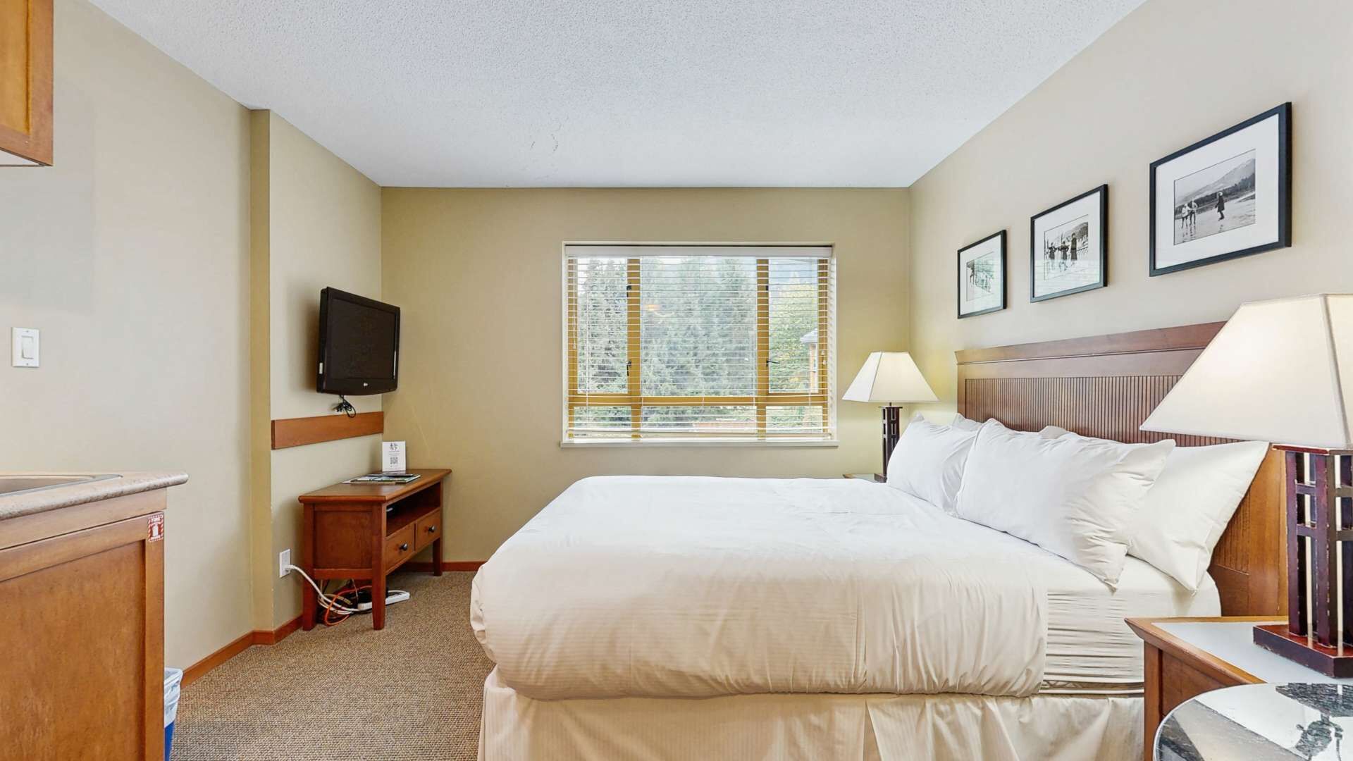 Ein Hotelzimmer mit einem Bett, Fernseher, Schreibtisch, Lampe und einem Fenster mit Jalousien.