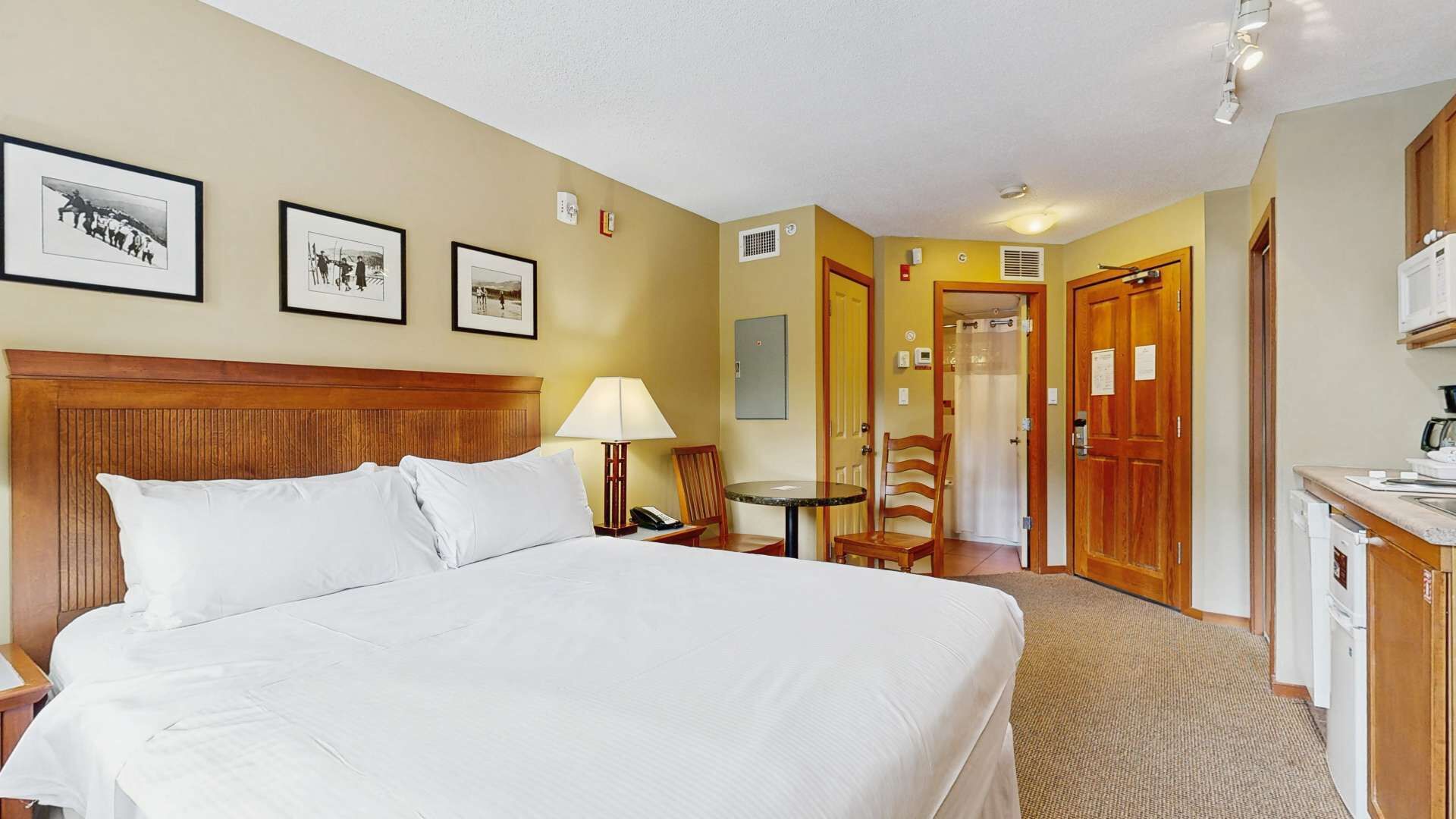 Hotelkamer met een groot bed, een bureau met lamp, een stoel, een kleine tafel en een kitchenette.
