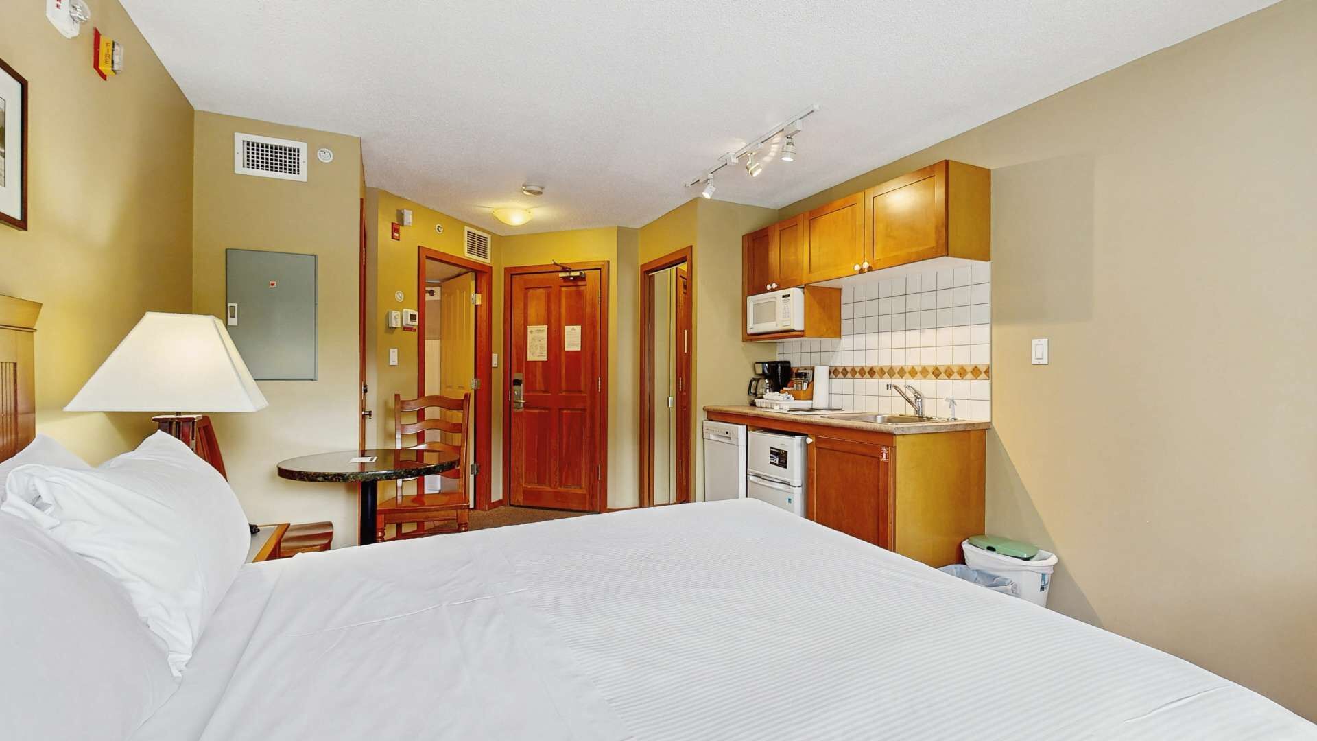 Een hotelkamer met een bed, een bureau, een stoel, een magnetron, een wastafel en een kleine keukenhoek.