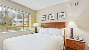 Une chambre d’hôtel avec un grand lit, deux tables de chevet avec des lampes et trois tableaux encadrés accrochés au mur.