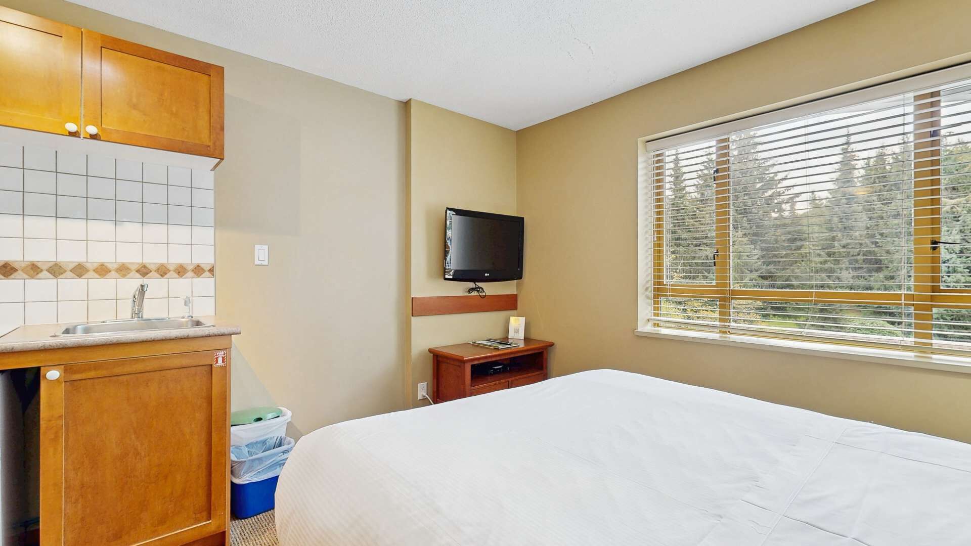 Une chambre d’hôtel avec un lit, une petite kitchenette, une télévision et une fenêtre avec des stores.