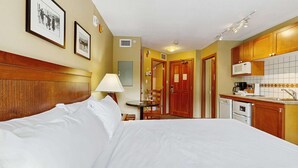 A hotel room with a bed, a desk, a chair, a lamp, a microwave, and a small kitchenette. - Whistler - Cascade Lodge 230 (Whistler)