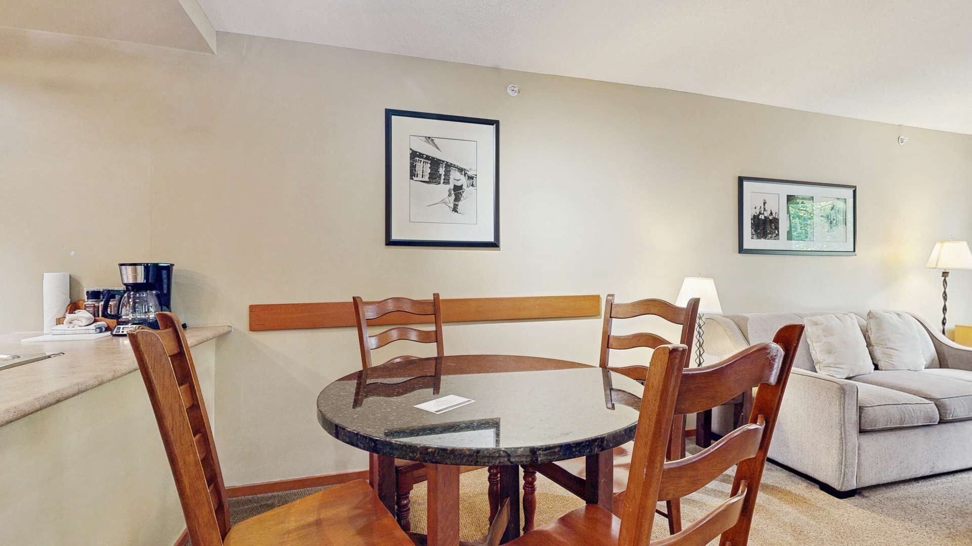 Un coin repas avec une table ronde et des chaises, un canapé et deux tableaux encadrés au mur.