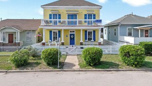 A two-story yellow house with a blue door, a balcony, and a picket fence. - Steps to Pleasure Pier: Family Escape w/ Pool! (Galveston)