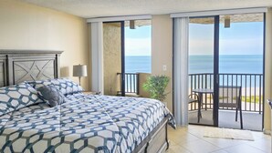 A bedroom with a large bed, a nightstand, a lamp, and a view of the ocean through a sliding glass door. - Walk to Sand Key! 11th-floor Clearwater Beach Gem (Clearwater Beach)