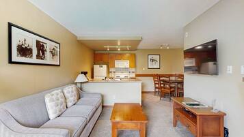 Un espacio habitable compacto con kitchenette, comedor y zona de estar con sofá y mesa de centro.