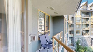 Un balcon avec une chaise, une fenêtre avec des stores et une vue sur les bâtiments voisins.