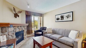 Un salon avec une cheminée en pierre, un fauteuil en cuir, un canapé gris et un tableau encadré au mur.