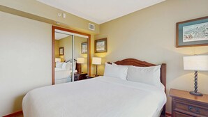 Une chambre d’hôtel avec un grand lit, une tête de lit en bois, une table de chevet avec une lampe, une commode, un miroir et un tableau encadré au mur.