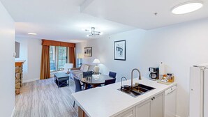 Une cuisine moderne dotée d’un îlot central, un coin repas avec une table et des chaises, et un espace salon avec un canapé et une machine à café.