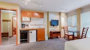 A compact hotel room with a kitchenette, a television, a dining area with a table and chairs, and a bed.