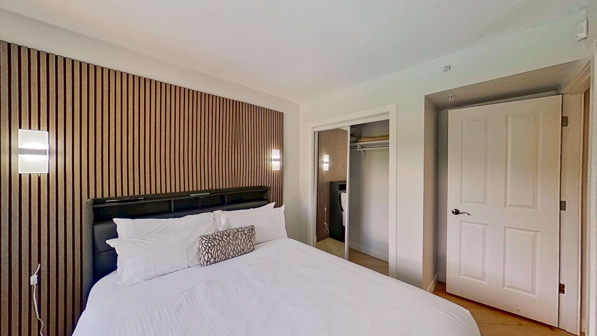 A hotel room with a large bed, a wooden headboard, and a walk-in closet with a white door.