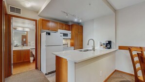 Eine kleine Küche mit Holzausstattung, einem weißen Kühlschrank, einer Mikrowelle, einem Spülbecken und einer Kaffeemaschine.