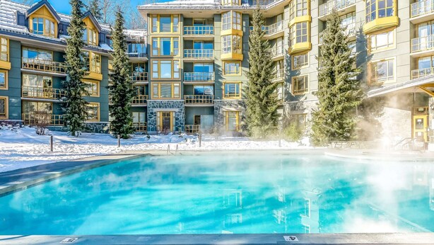 Ein Hotel mit einem großen Außenpool, umgeben von Schnee, mit mehrstöckigen Gebäuden, Balkonen und großen Fenstern.