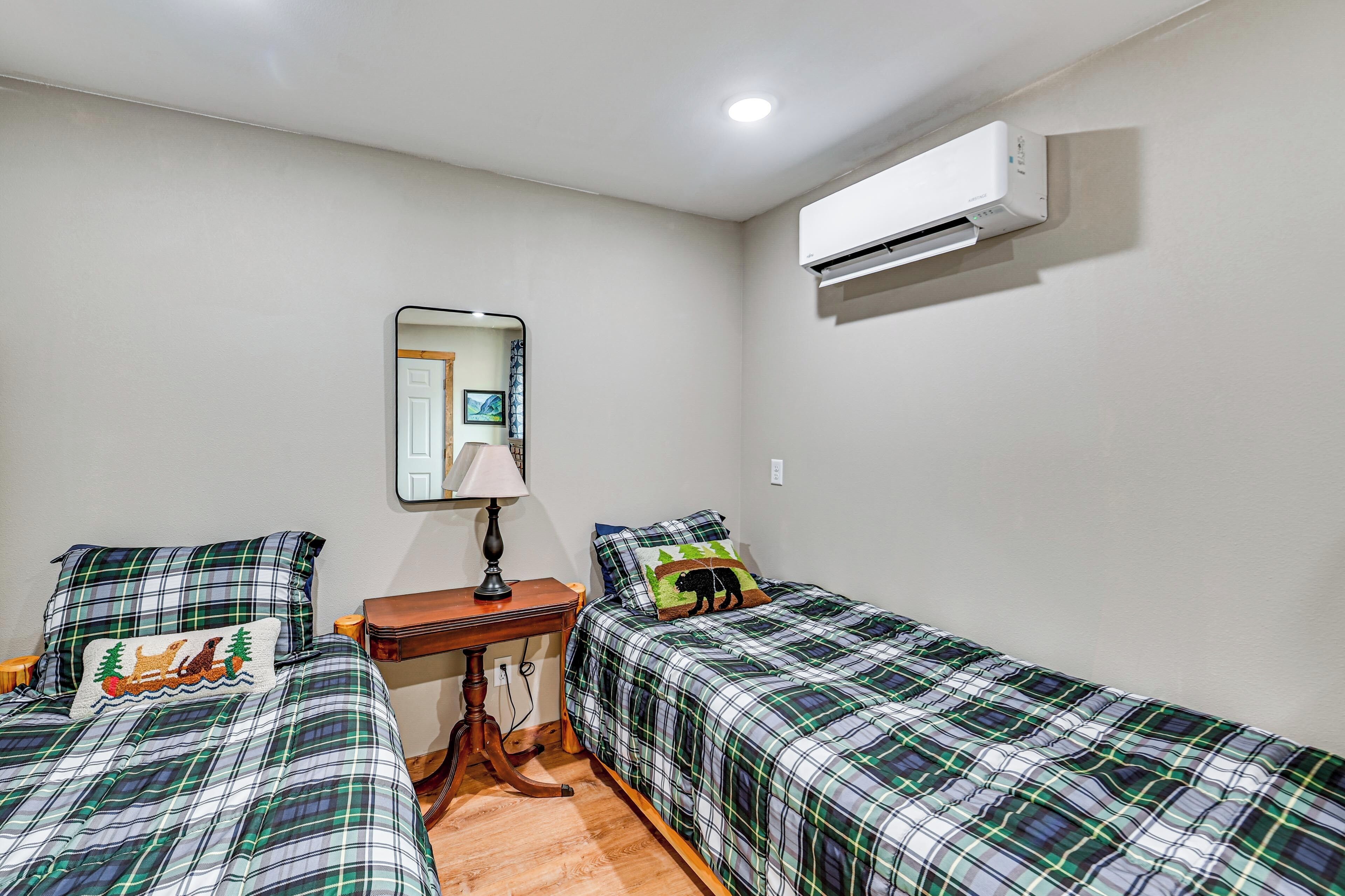 Un dormitorio con dos camas, una mesita de noche, una lámpara, aire acondicionado y un espejo en la pared.