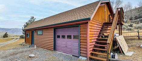 A log cabin with a purple garage door, a wooden staircase, and a gravel driveway.