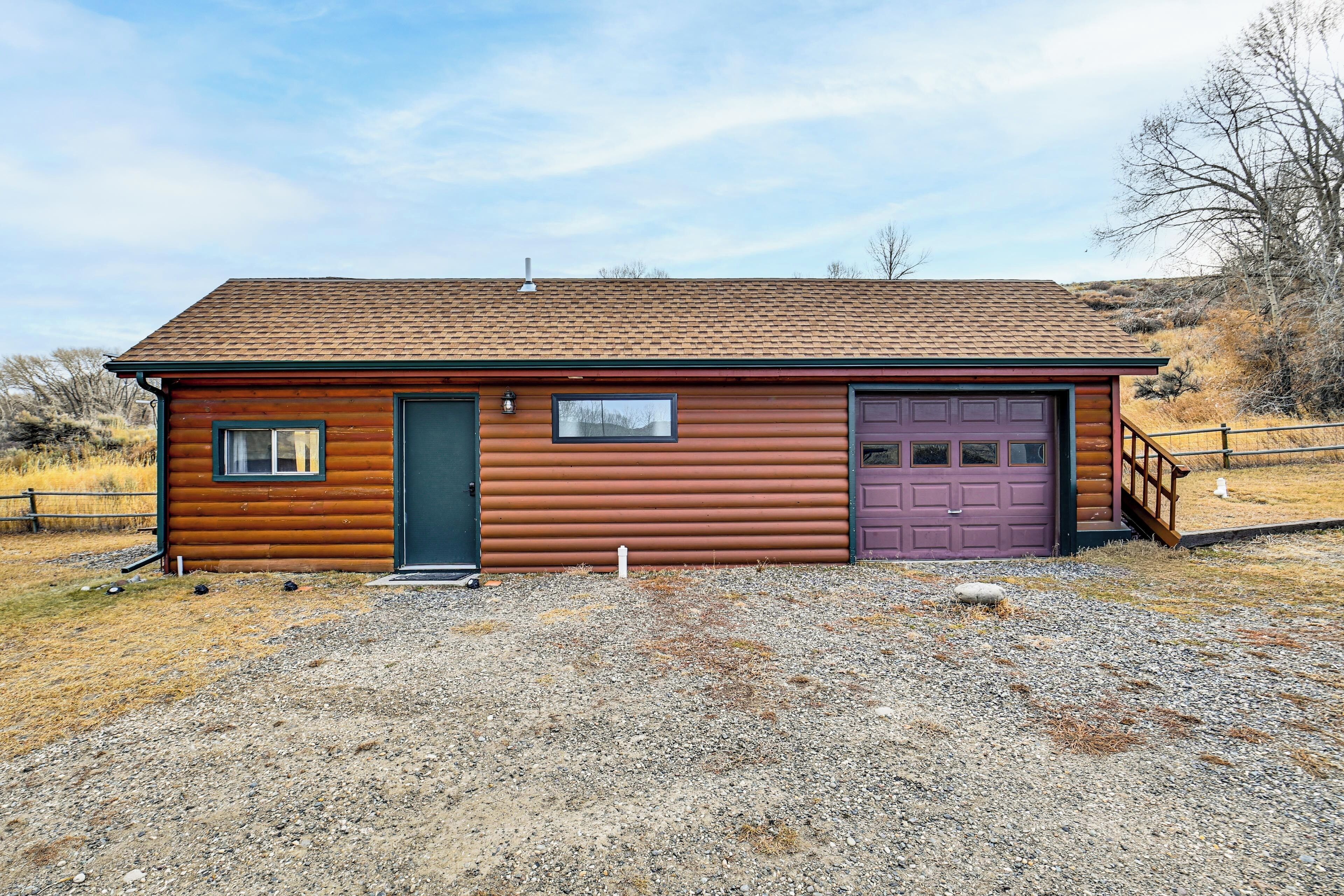 A single-story log cabin with a dark brown exterior, a purple garage door, and a gravel driveway.