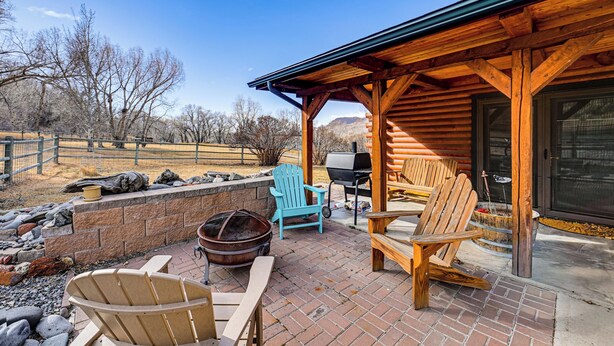 Een houten chalet met een terras, Adirondack stoelen, een vuurkorf en een barbecue.