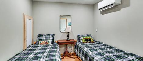 Un dormitorio con dos camas, una mesita de noche de madera, un espejo y un equipo de aire acondicionado.
