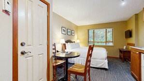 Una habitación de hotel con cama, mesita de noche, lámpara, silla y una ventana con persianas.
