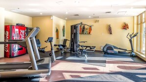 Un gimnasio con máquinas de cardio, equipo de entrenamiento con pesas y un refrigerador de Coca-Cola.