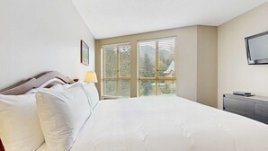 Ein Schlafzimmer mit einem großen Bett, einem Nachttisch mit Lampe, einem an der Wand befestigten Fernseher und einem Fenster mit Jalousien.
