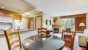 Eine moderne Küche mit Herd, Mikrowelle und Kühlschrank. Ein Essbereich mit rundem Tisch und Stühlen ist vorhanden. Im Hintergrund ist ein Kamin zu sehen.