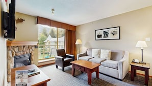 Ein gemütliches Wohnzimmer mit Kamin aus Stein, einer Couch, einem Couchtisch und einem an der Wand montierten Fernseher.