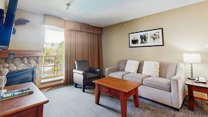 Une chambre d’hôtel avec une cheminée en pierre, un canapé, un fauteuil, une table basse et une photo encadrée accrochée au mur.