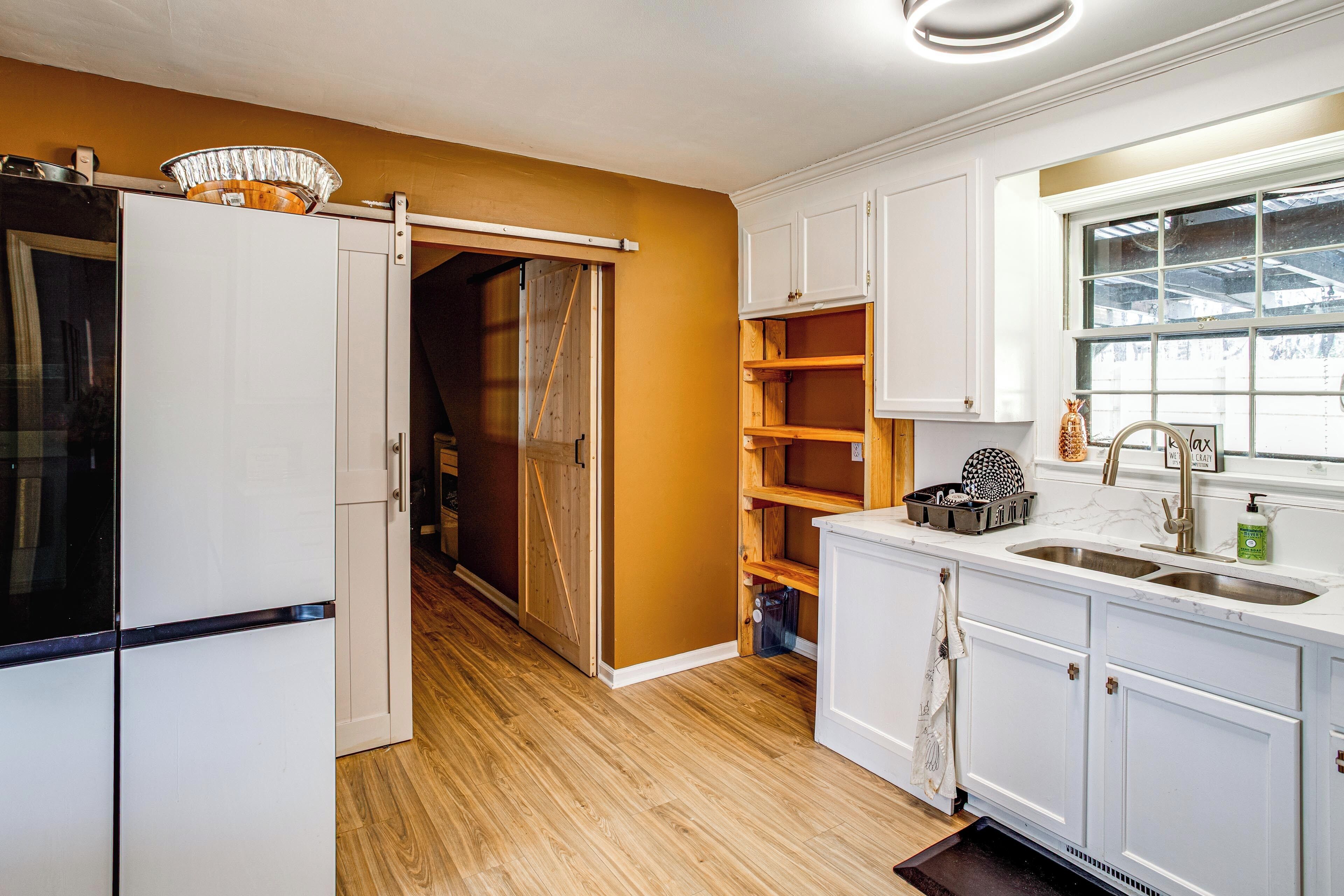 A kitchen with white cabinets, a wooden floor, and a window with a view.