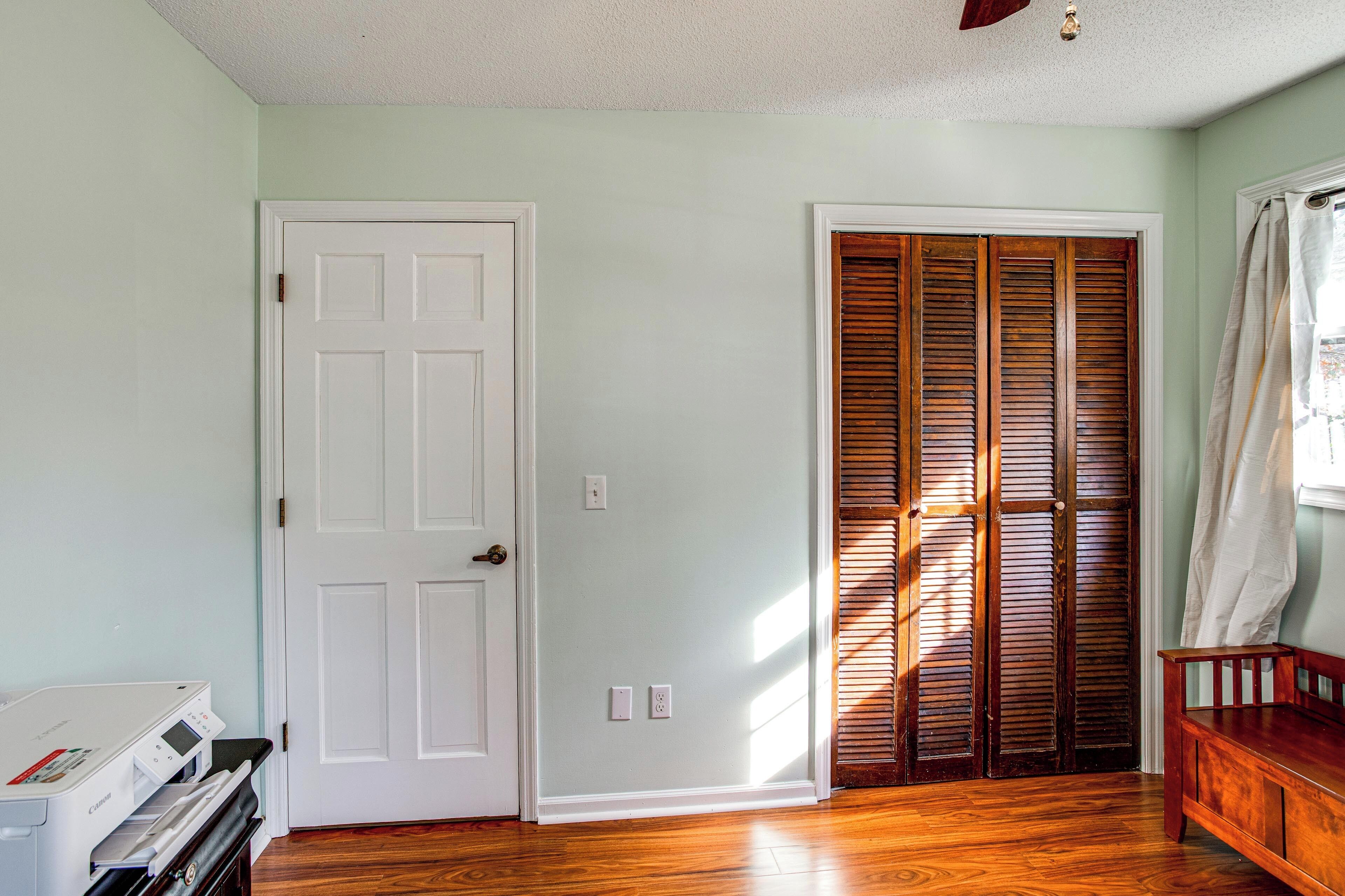 A room with a white door, a wooden bench, and a wooden closet with louvered doors.