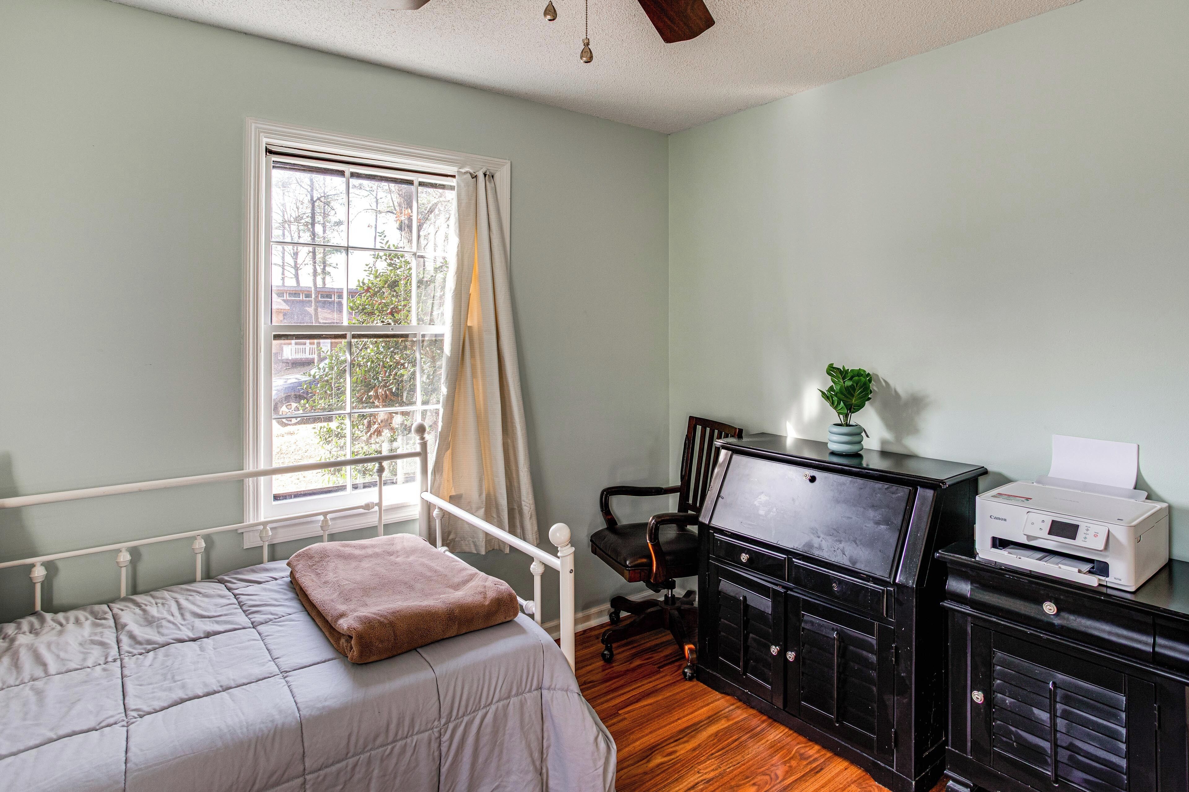 A bedroom with a bed, a desk with a printer, a chair, and a window with curtains.