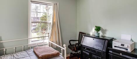 A bedroom with a bed, a desk with a printer, a chair, and a window with curtains.