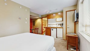 Een kleine hotelkamer met een enkel bed, een kitchenette en een badkamer die door een open deur zichtbaar is.