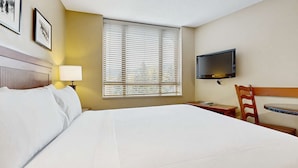 Ein Hotelzimmer mit Bett, Schreibtisch, Stuhl, Fernseher und einem Fenster mit Jalousien.