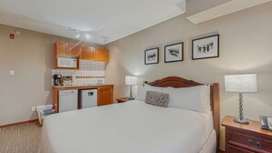 Ein Hotelzimmer mit einem Bett, Nachttischen, einem Schreibtisch mit Mikrowelle, Kühlschrank und einer kleinen Küchenzeile. An der Wand hängen drei gerahmte Bilder.