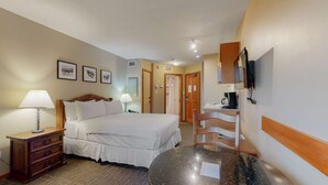 Ein Hotelzimmer mit einem Bett, zwei Nachttischen mit Lampen, einer Holzkommode, einem runden Marmortisch, einem an der Wand montierten Fernseher und gerahmten Bildern.