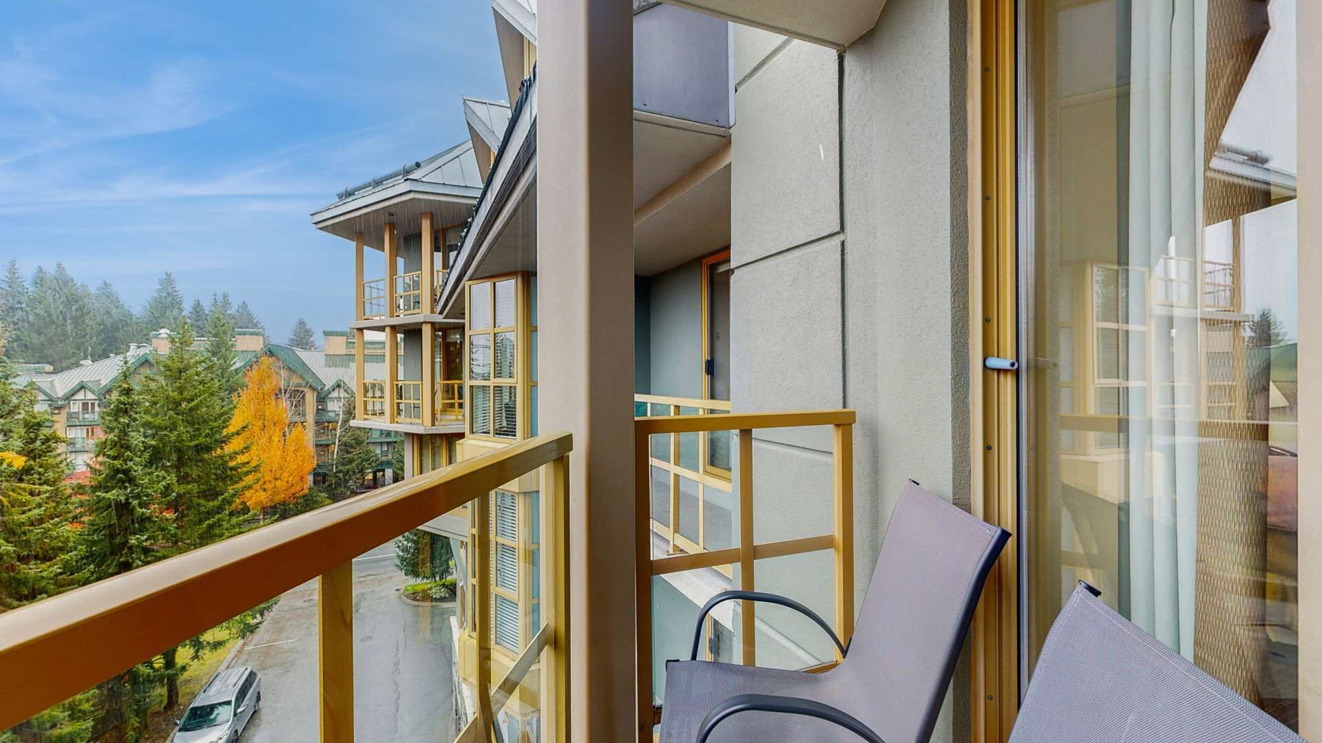 A balcony with a view of a residential area, a chair, and a window with a view of a car on the street.