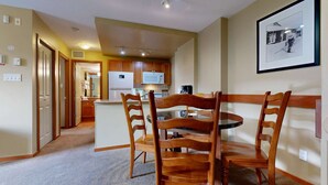 Un coin repas avec une table ronde et des chaises en bois, une cuisine à l’arrière-plan et un tableau encadré au mur.