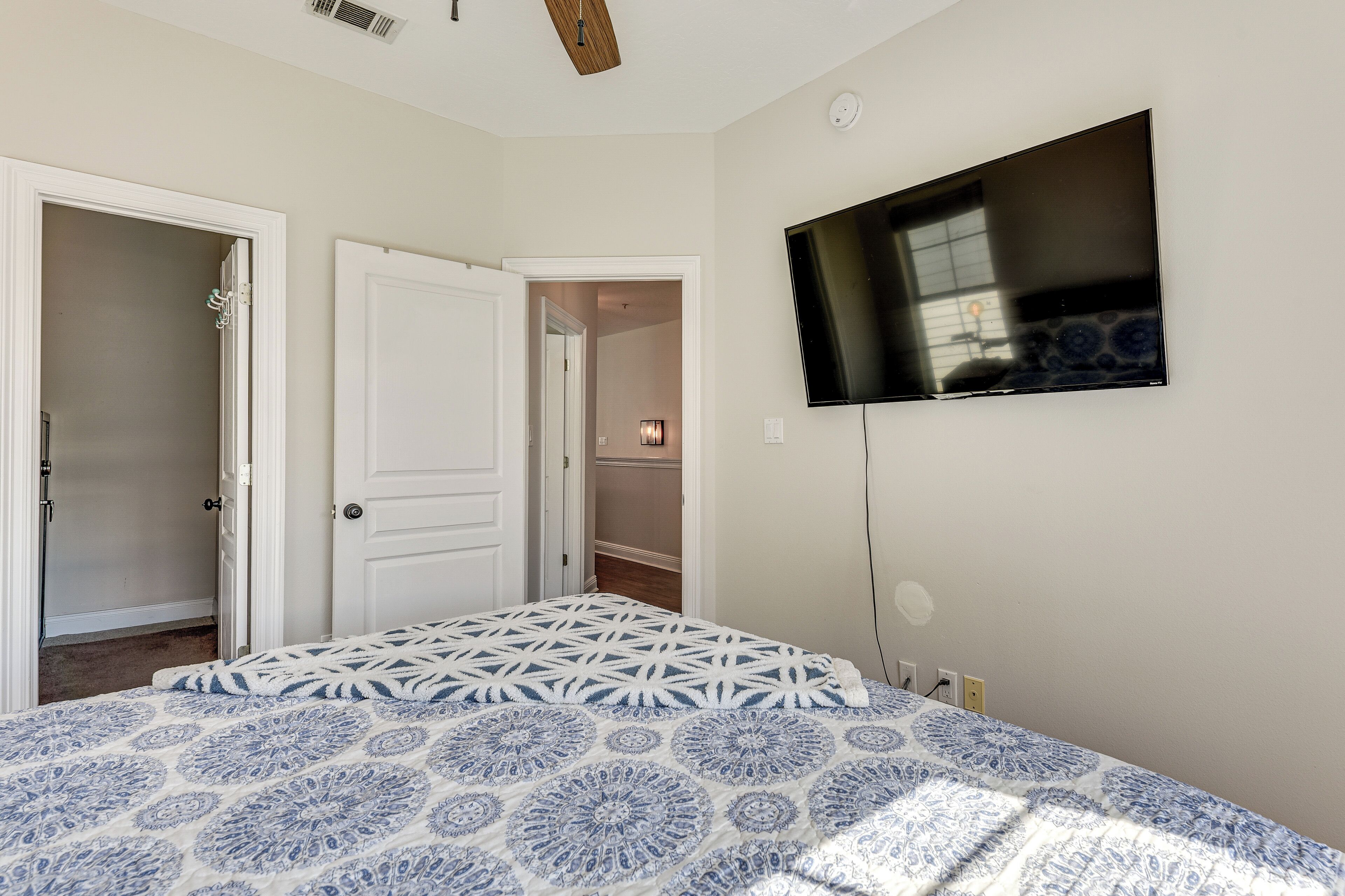 A bedroom with a bed, a TV mounted on the wall, and a door leading to another room.